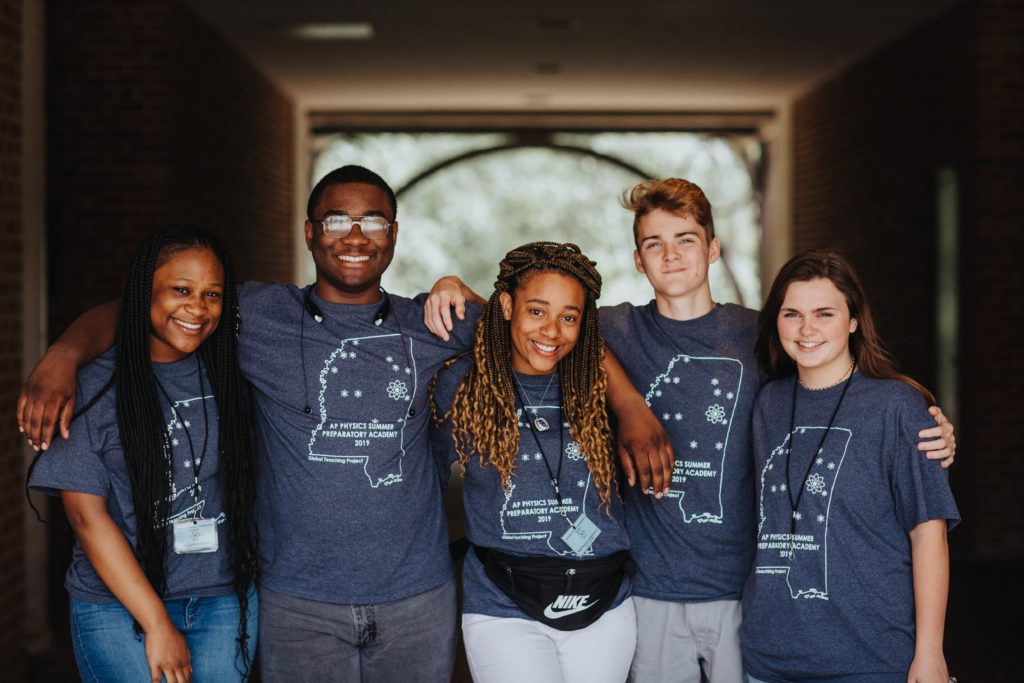 Five students stand with arms over one another's shoulders on the MSU campus.