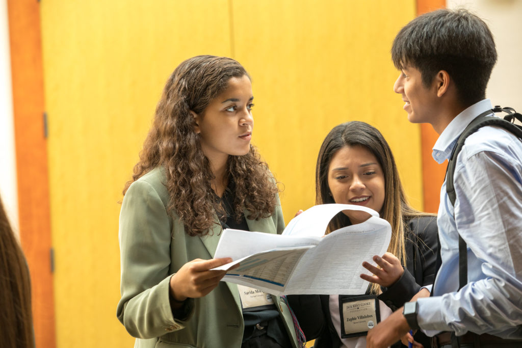 Three students in conversation in front of a bright yellow wall