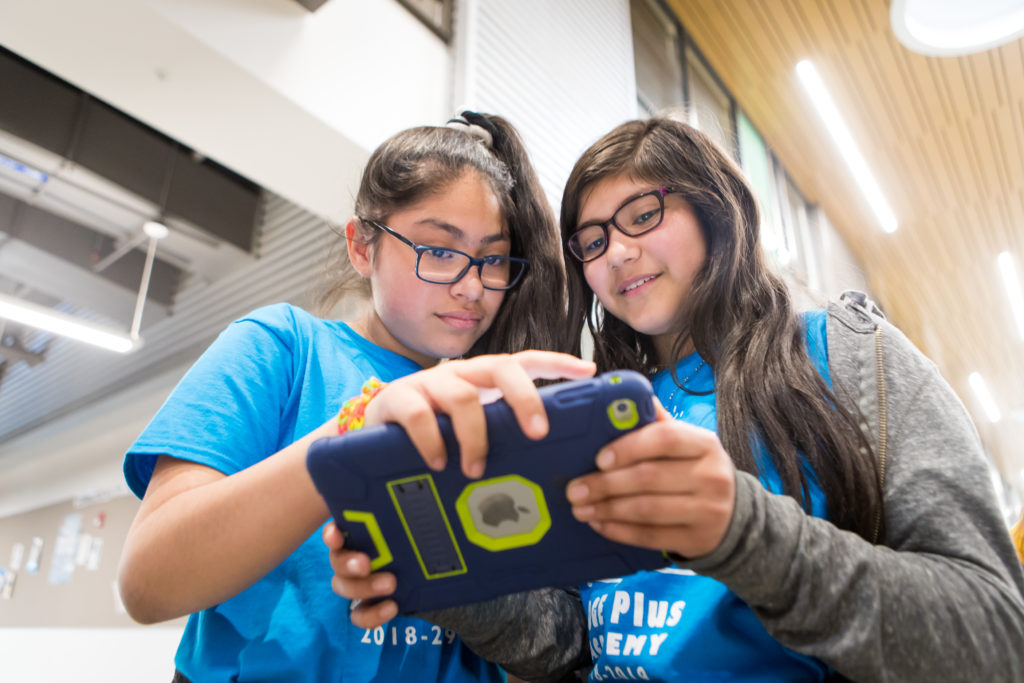 Two girls hold an iPad together.