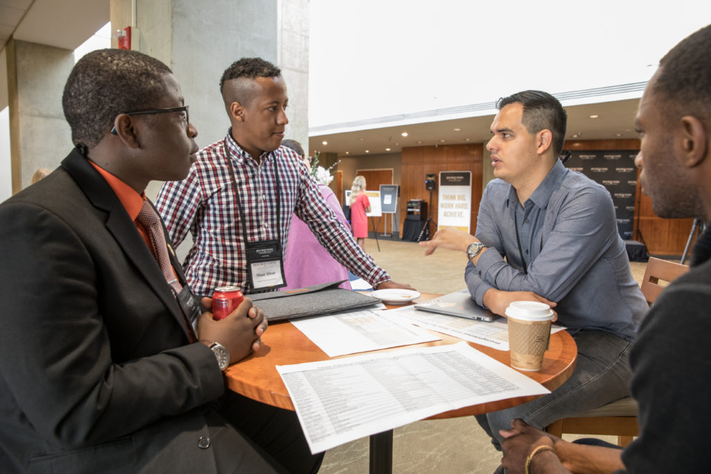 Three young, professionally-dressed students sitting and talking at a table.