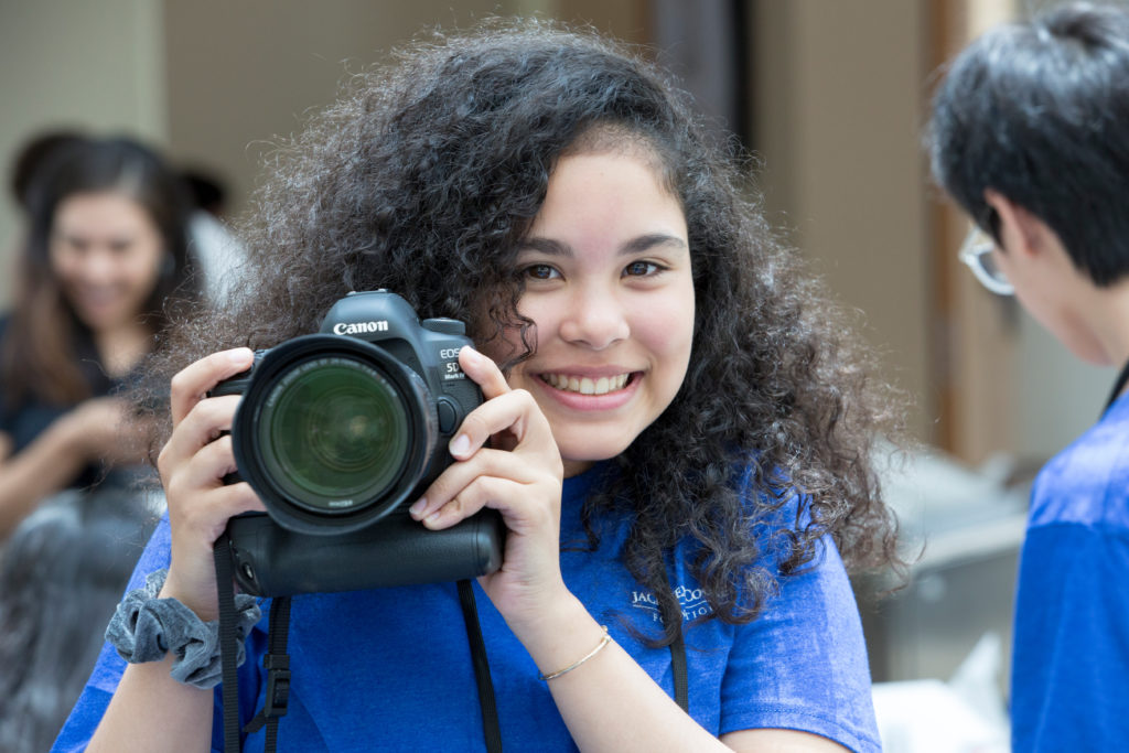 A middle grade girl smiles big and holds a camera