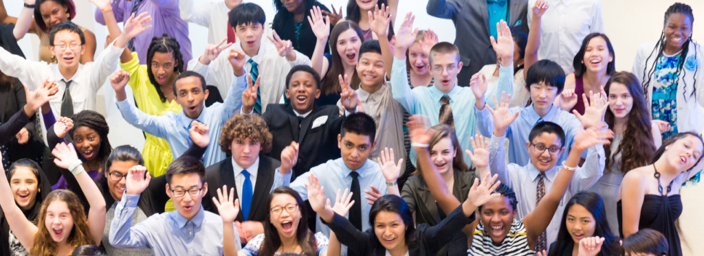A large group of middle school students cheers. They are wearing formal attire.